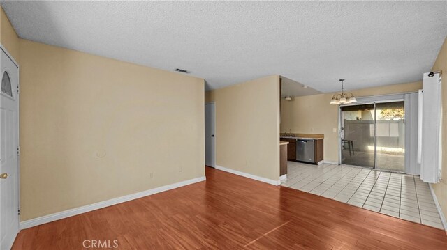 unfurnished living room featuring a textured ceiling, light hardwood / wood-style flooring, and a notable chandelier