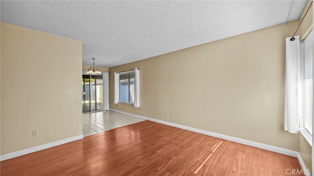 unfurnished room featuring a notable chandelier, a textured ceiling, and light hardwood / wood-style flooring