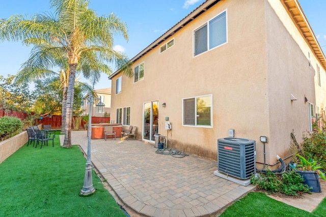 rear view of house with a lawn, cooling unit, a patio, and a hot tub