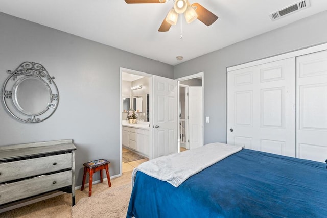 bedroom with a closet, light colored carpet, ensuite bath, and ceiling fan