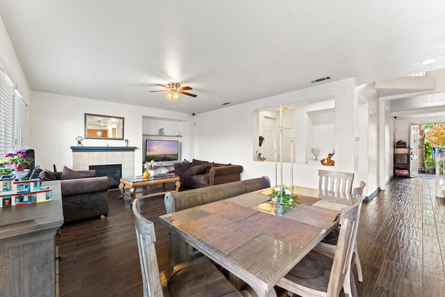 dining area with a tile fireplace, ceiling fan, and dark hardwood / wood-style flooring