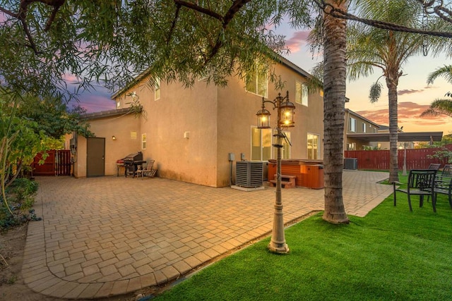 back house at dusk with a patio, a hot tub, and cooling unit