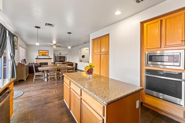 kitchen featuring appliances with stainless steel finishes, light stone counters, dark hardwood / wood-style floors, a kitchen island, and a tiled fireplace