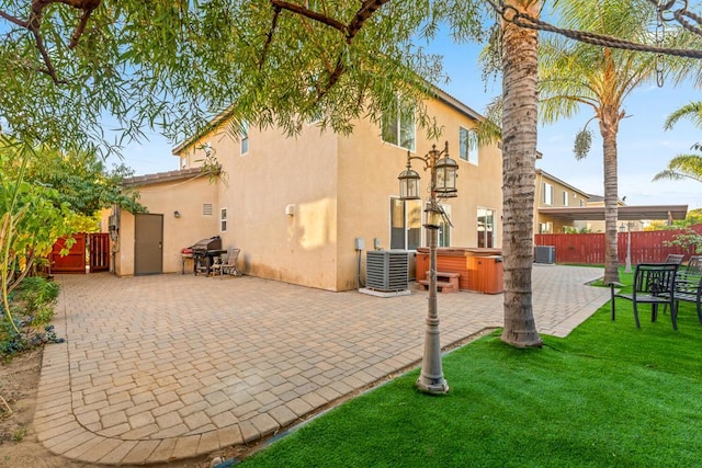 back of property with central AC, a patio area, and a hot tub