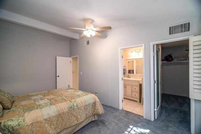 bedroom featuring ensuite bathroom, ceiling fan, a closet, light colored carpet, and a walk in closet