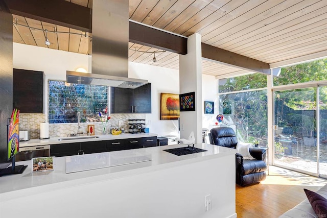 kitchen with sink, island exhaust hood, expansive windows, backsplash, and beam ceiling