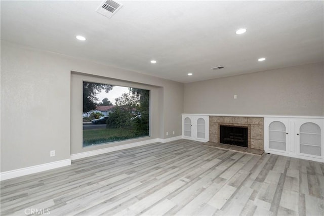 unfurnished living room with light wood-type flooring and a tile fireplace