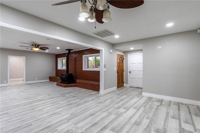 unfurnished living room with light hardwood / wood-style floors, a wood stove, ceiling fan, and brick wall