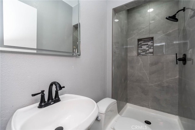 bathroom featuring tiled shower, toilet, and sink