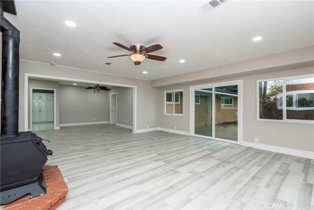 unfurnished living room with a wood stove, ceiling fan, and light wood-type flooring