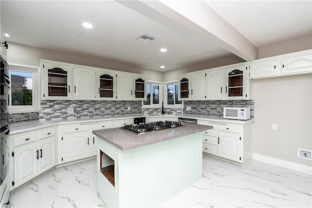 kitchen featuring white cabinetry, a center island, sink, stainless steel gas cooktop, and tasteful backsplash