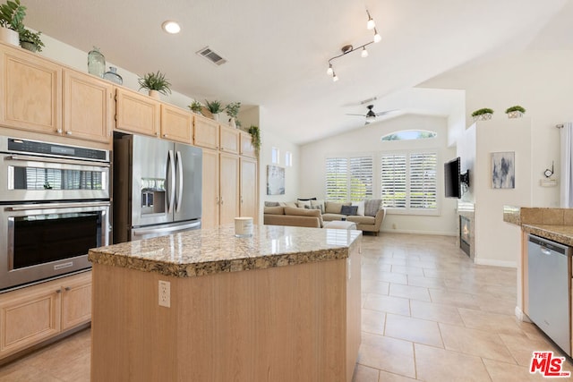 kitchen with light stone counters, stainless steel appliances, vaulted ceiling, light brown cabinets, and a kitchen island