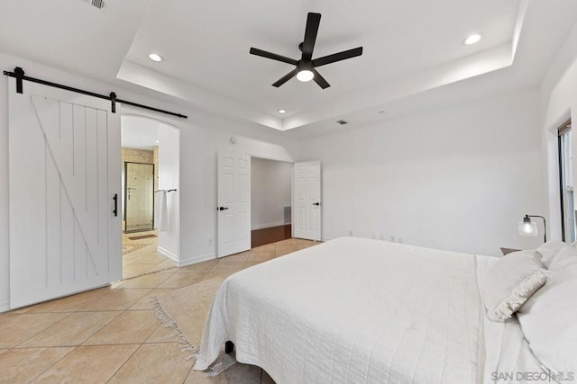 bedroom featuring connected bathroom, a barn door, ceiling fan, and a tray ceiling