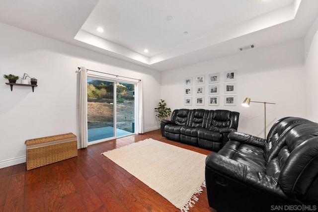 living room with a raised ceiling and dark wood-type flooring