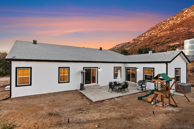 back house at dusk featuring a mountain view, a patio area, and a playground