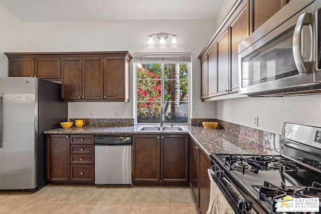 kitchen featuring appliances with stainless steel finishes, dark stone countertops, dark brown cabinetry, and sink