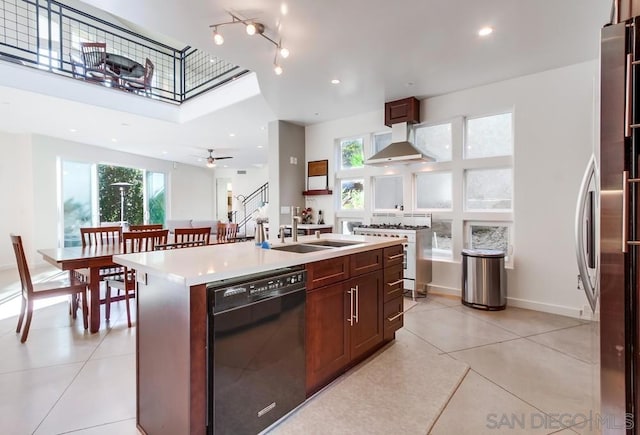 kitchen featuring wall chimney range hood, sink, a center island with sink, black dishwasher, and stainless steel stove