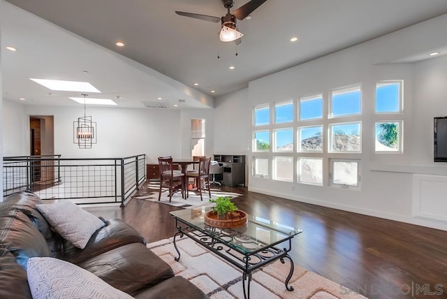 living room with ceiling fan with notable chandelier, dark hardwood / wood-style flooring, and a skylight