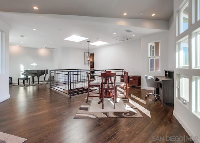 dining area featuring a towering ceiling, a skylight, dark wood-type flooring, and a notable chandelier