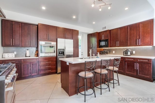 kitchen with light tile patterned floors, stainless steel appliances, a kitchen island with sink, and a breakfast bar area