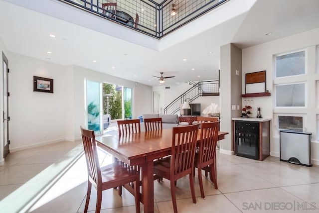 dining space with light tile patterned floors, a towering ceiling, beverage cooler, and ceiling fan