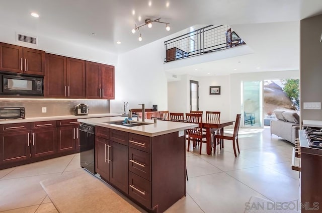 kitchen featuring a kitchen island with sink, black appliances, sink, decorative backsplash, and light tile patterned floors