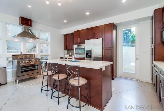 kitchen featuring a breakfast bar, stainless steel appliances, sink, wall chimney range hood, and an island with sink