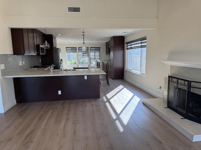 kitchen with stainless steel appliances, tasteful backsplash, kitchen peninsula, pendant lighting, and light hardwood / wood-style floors