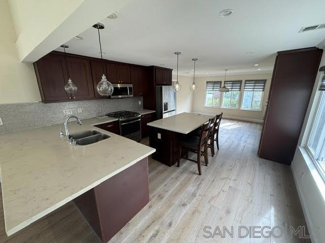 kitchen with pendant lighting, sink, light hardwood / wood-style flooring, a kitchen bar, and stainless steel appliances