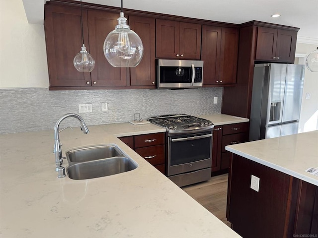 kitchen featuring backsplash, sink, light wood-type flooring, appliances with stainless steel finishes, and decorative light fixtures