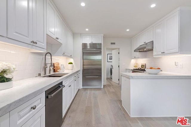 kitchen featuring sink, light hardwood / wood-style floors, decorative backsplash, white cabinets, and appliances with stainless steel finishes