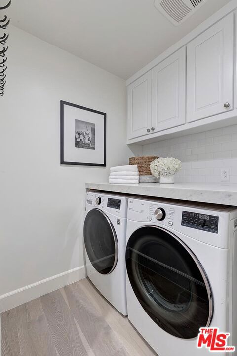 laundry room with washing machine and dryer, light hardwood / wood-style flooring, and cabinets