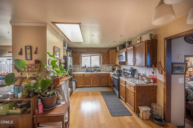 kitchen featuring tile counters, tasteful backsplash, light wood-type flooring, appliances with stainless steel finishes, and ornamental molding