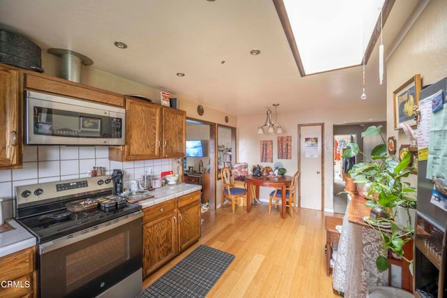 kitchen featuring tasteful backsplash, stainless steel appliances, tile countertops, light hardwood / wood-style floors, and hanging light fixtures