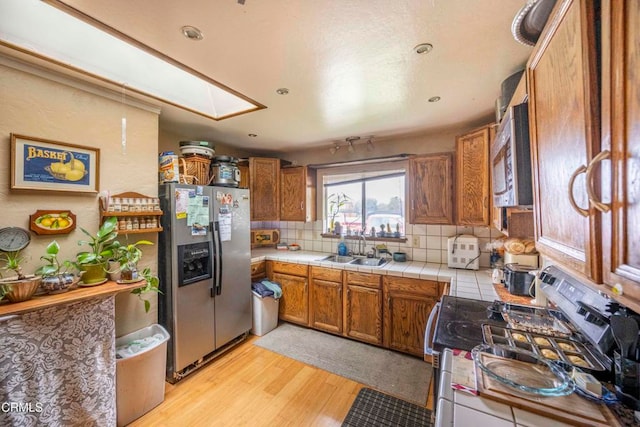 kitchen featuring tile countertops, a skylight, decorative backsplash, light hardwood / wood-style floors, and stainless steel appliances