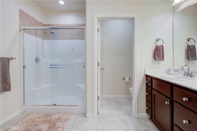 bathroom featuring toilet, a stall shower, vanity, baseboards, and tile patterned floors