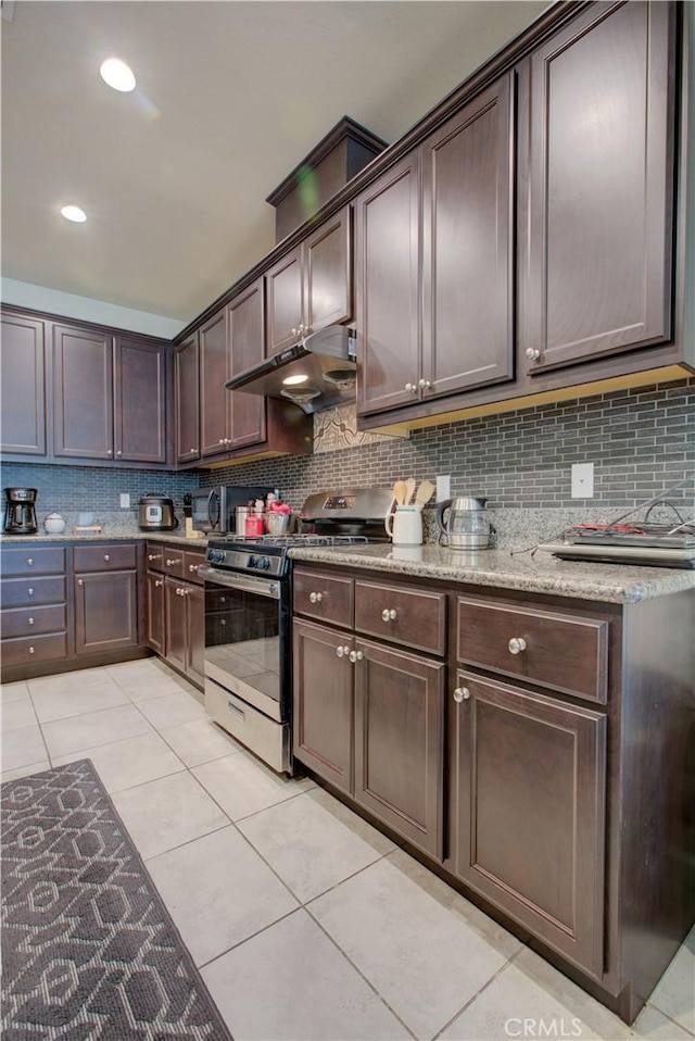 kitchen with dark brown cabinetry, tasteful backsplash, under cabinet range hood, and gas stove