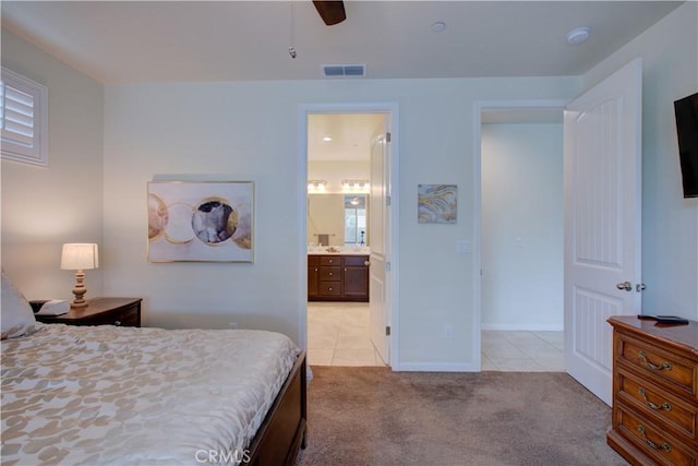 bedroom featuring light tile patterned floors, visible vents, light carpet, ceiling fan, and ensuite bath