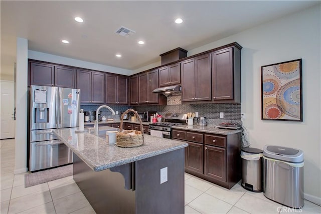 kitchen with visible vents, appliances with stainless steel finishes, an island with sink, light stone countertops, and under cabinet range hood