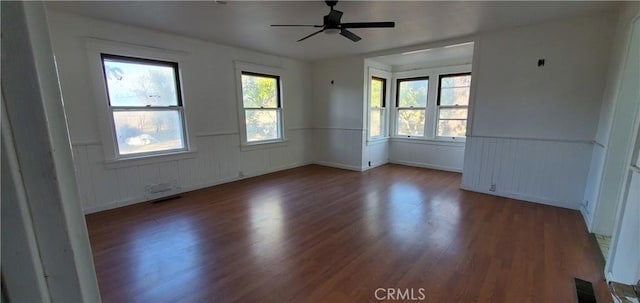 empty room with plenty of natural light, wood finished floors, and a wainscoted wall