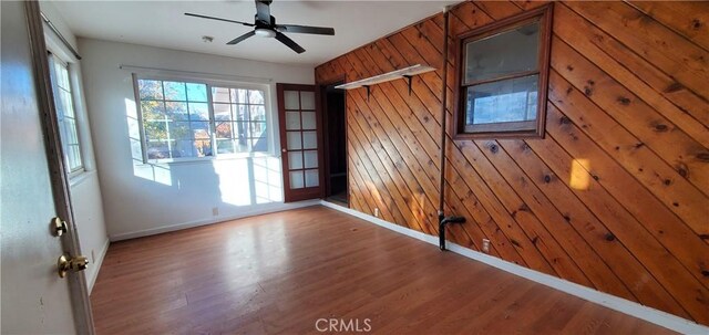spare room with a ceiling fan, wooden walls, wood finished floors, and baseboards