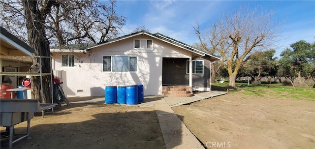 rear view of property featuring crawl space and stucco siding