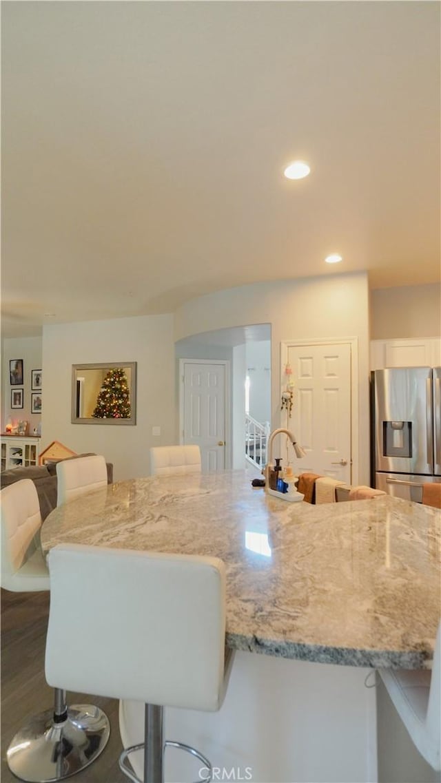 kitchen with hardwood / wood-style floors, a breakfast bar, light stone counters, and stainless steel refrigerator with ice dispenser