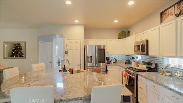 kitchen with a kitchen bar, light stone countertops, stainless steel appliances, and a kitchen island with sink