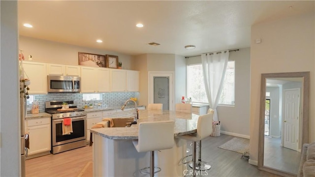 kitchen with light stone countertops, a kitchen breakfast bar, appliances with stainless steel finishes, white cabinets, and light wood-type flooring