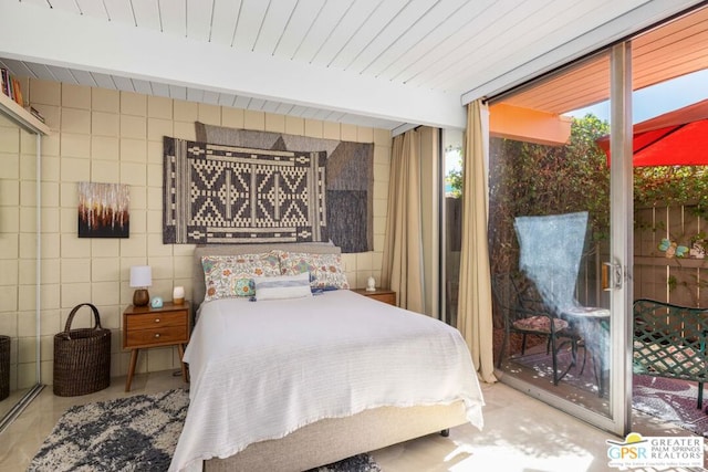 bedroom featuring beam ceiling, a wall of windows, and tile walls