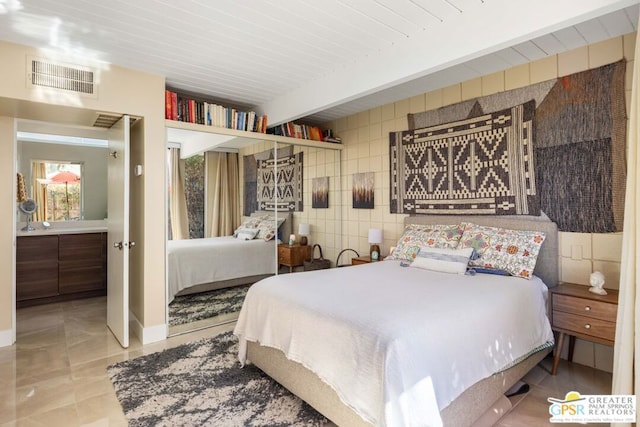 bedroom featuring light tile patterned floors, tile walls, and beamed ceiling