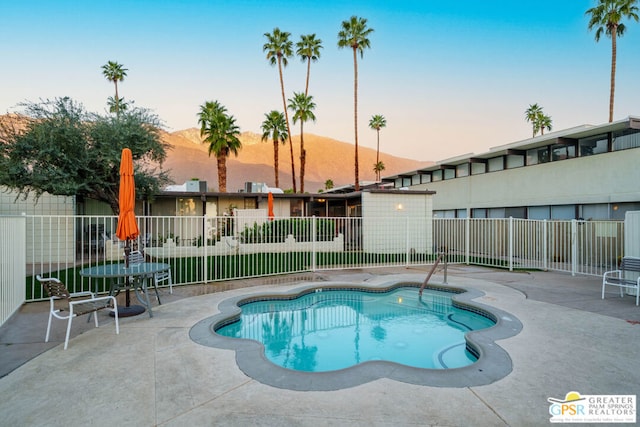 pool at dusk featuring a mountain view and a patio