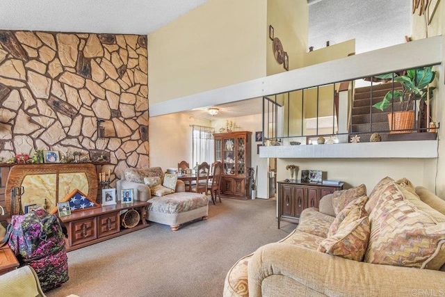 living room with a towering ceiling, a textured ceiling, carpet flooring, and a stone fireplace