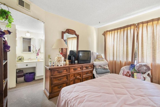 carpeted bedroom with a textured ceiling, ensuite bath, and visible vents